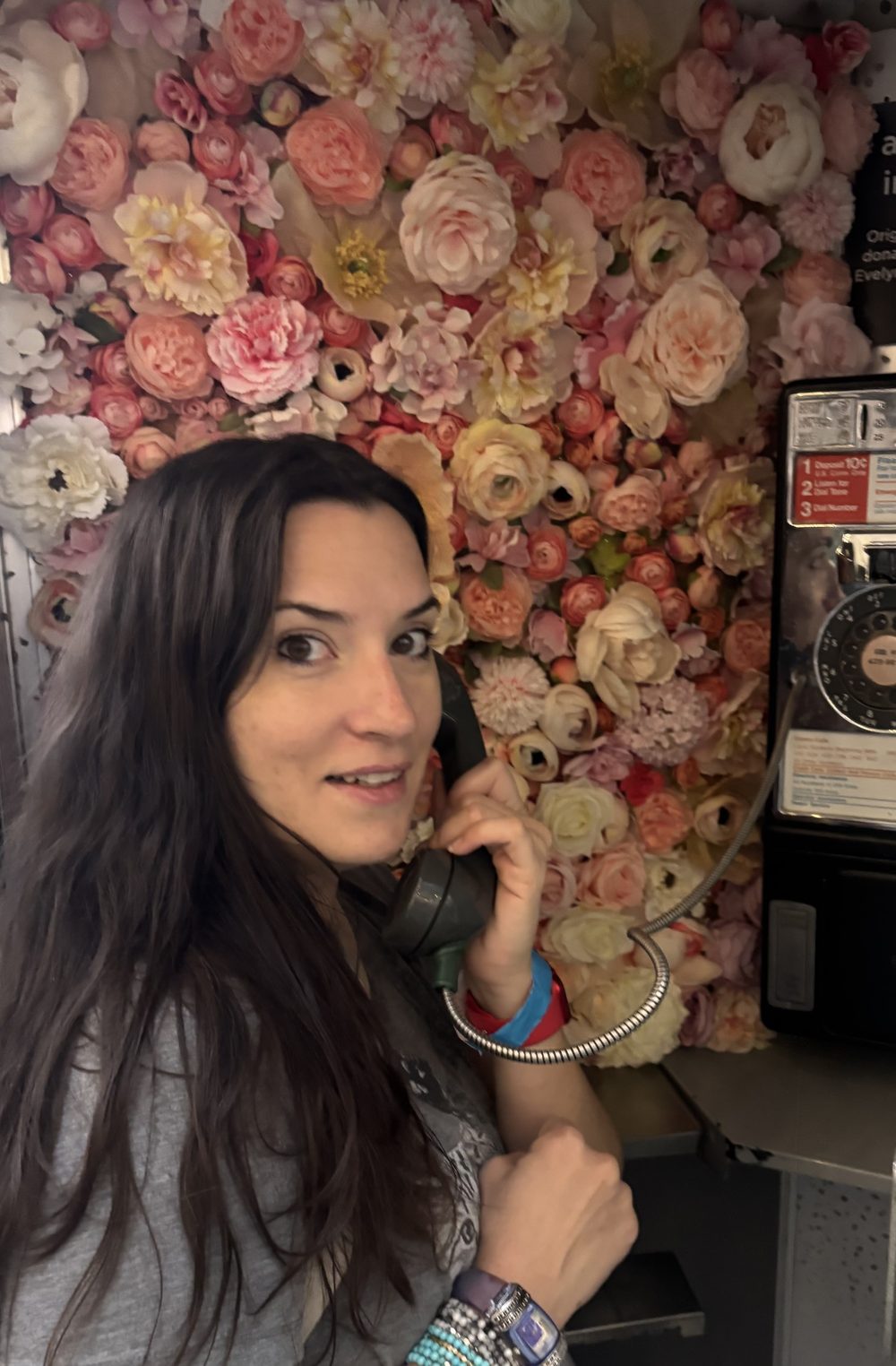 Amber Reed on a vintage payphone in front of a wall of flowers